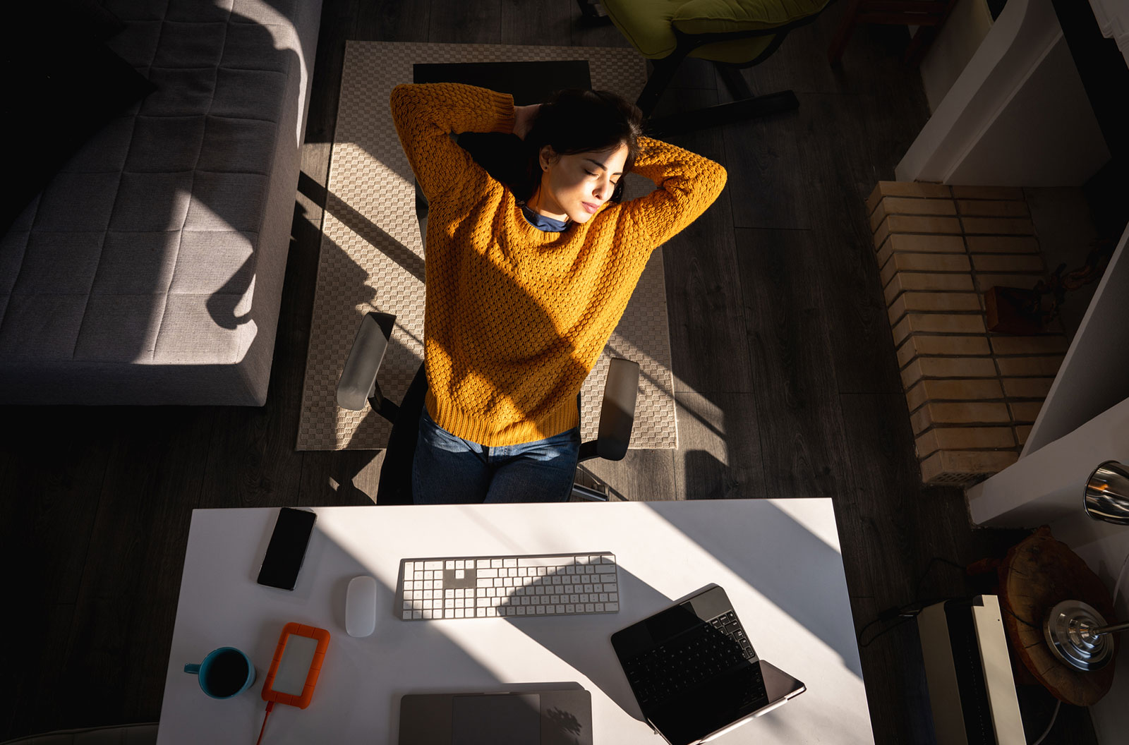 A young woman with closed eyes sitting on chair with hands behind head and taking break while working from home