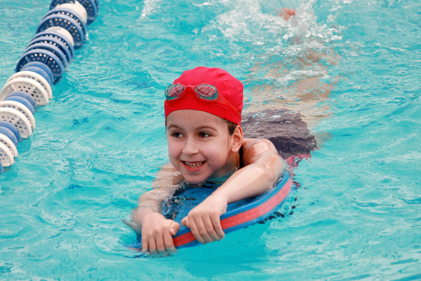 Deklica, ki obiskuje plavalni tečaj za otroke, v bazenu čofota z učnim pripomočkom