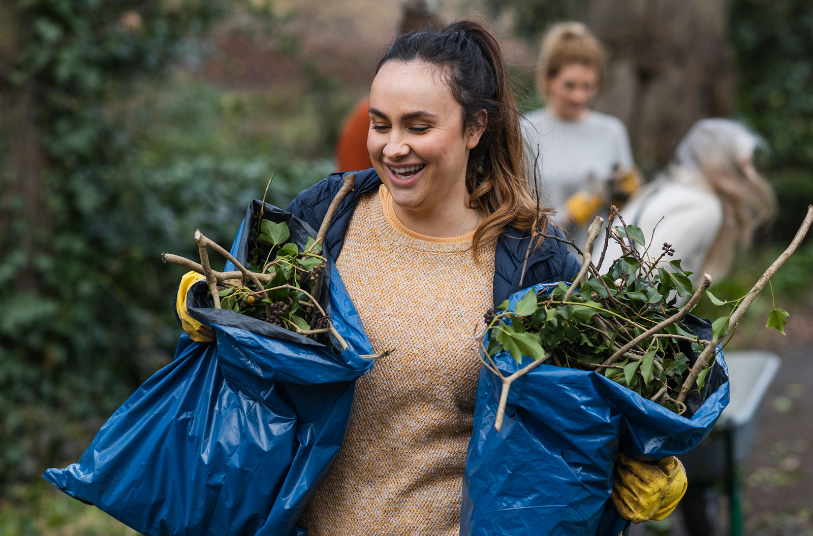 A woman smiling while carrying two bags of foliage. 