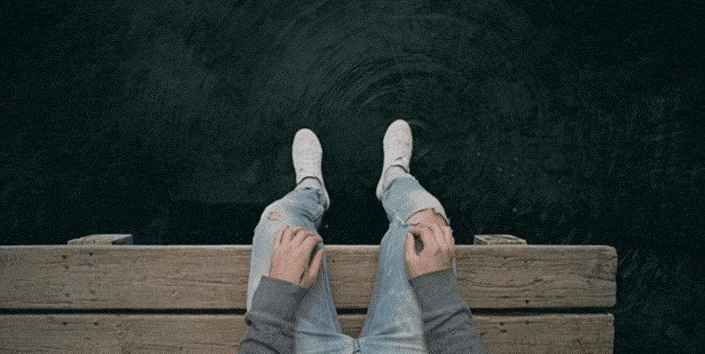 Gif of a person sitting on a boardwalk by the lake, tapping the water with his foot